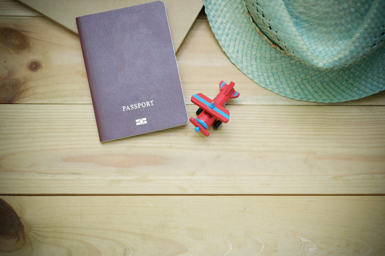 gallery-2 Flat lay of a passport, straw hat, and toy airplane on a wooden surface.