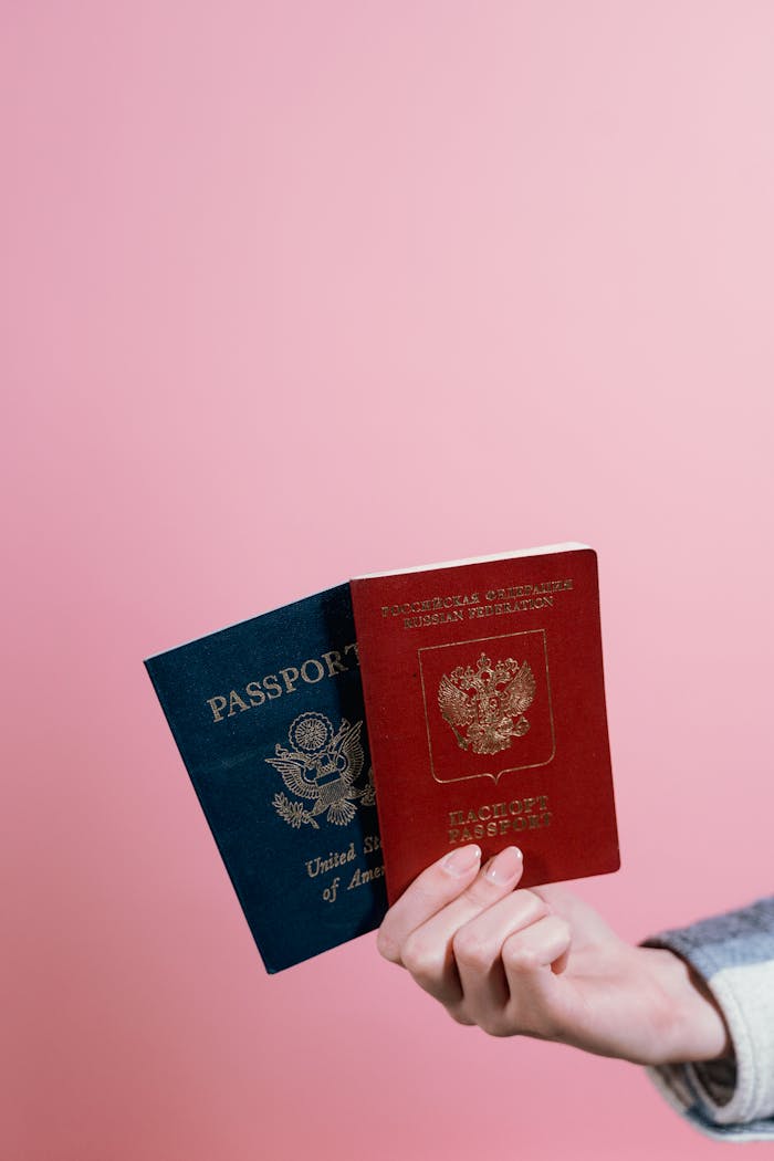 gallery-5 Close-up of two passports held by a hand against a pink background.