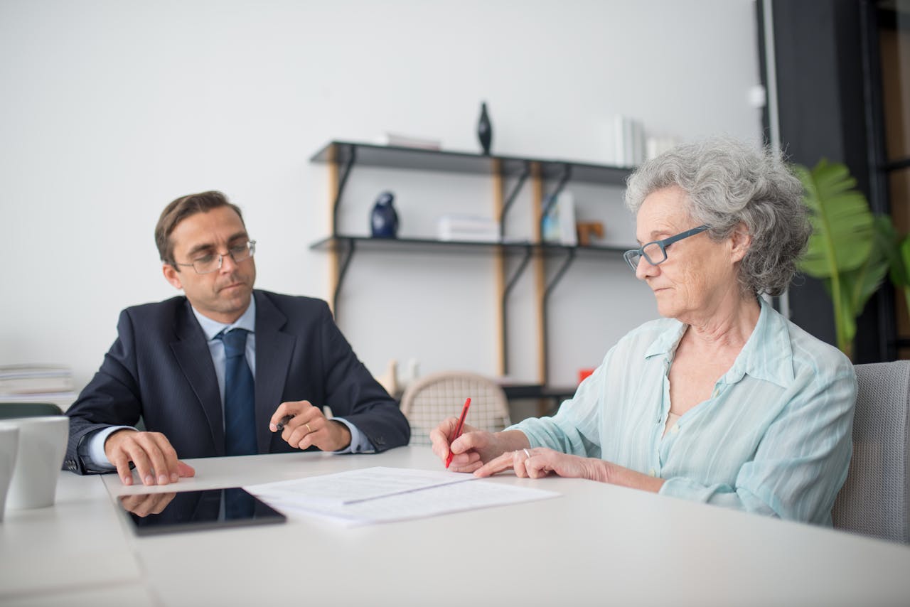 services-img Elderly woman signing paperwork in modern office with consultant.